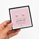 Heart-shaped earrings in a box with humorous message, held by a hand.