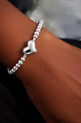 Silver heart-shaped bracelet on a wrist with a blurred background