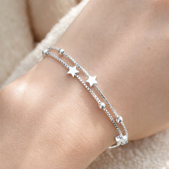 Silver bracelet with star charms on a wrist against a neutral background