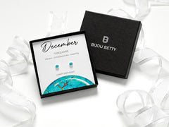 Sterling silver December birthstone earrings with 4mm turquoise cubic zirconia. Perfect gift for daughters, sisters, granddaughters, nieces, or friends. Includes gift box, bag, tissue, and card with characteristics: vibrant, compassionate, inspiring.