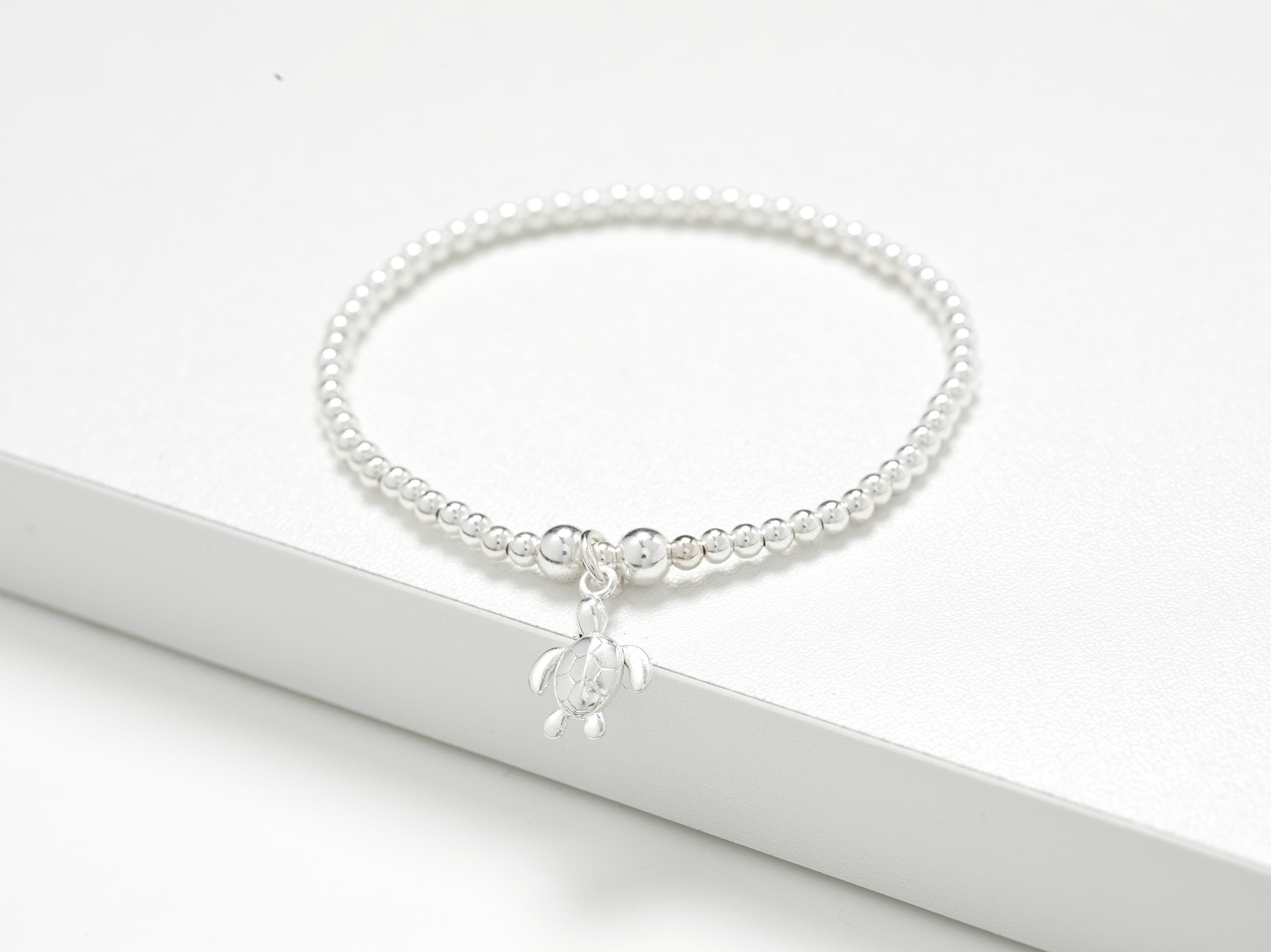 Solid sterling silver turtle charm stretch bead bracelet. Presented in luxury gift packaging which includes gift box, matching bag, tissue paper and ribbon.