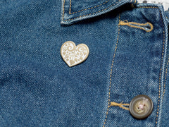 Bijou Betty’s gold-plated heart enamel pin with floral motif, pinned to a denim jacket, showcasing its 26mm x 25mm size.
