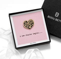 Close-up of Bijou Betty’s gold-plated heart enamel pin, 26mm x 25mm, with white floral motif, displayed against a white background.