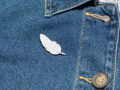 Enamel feather pin on denim jacket.