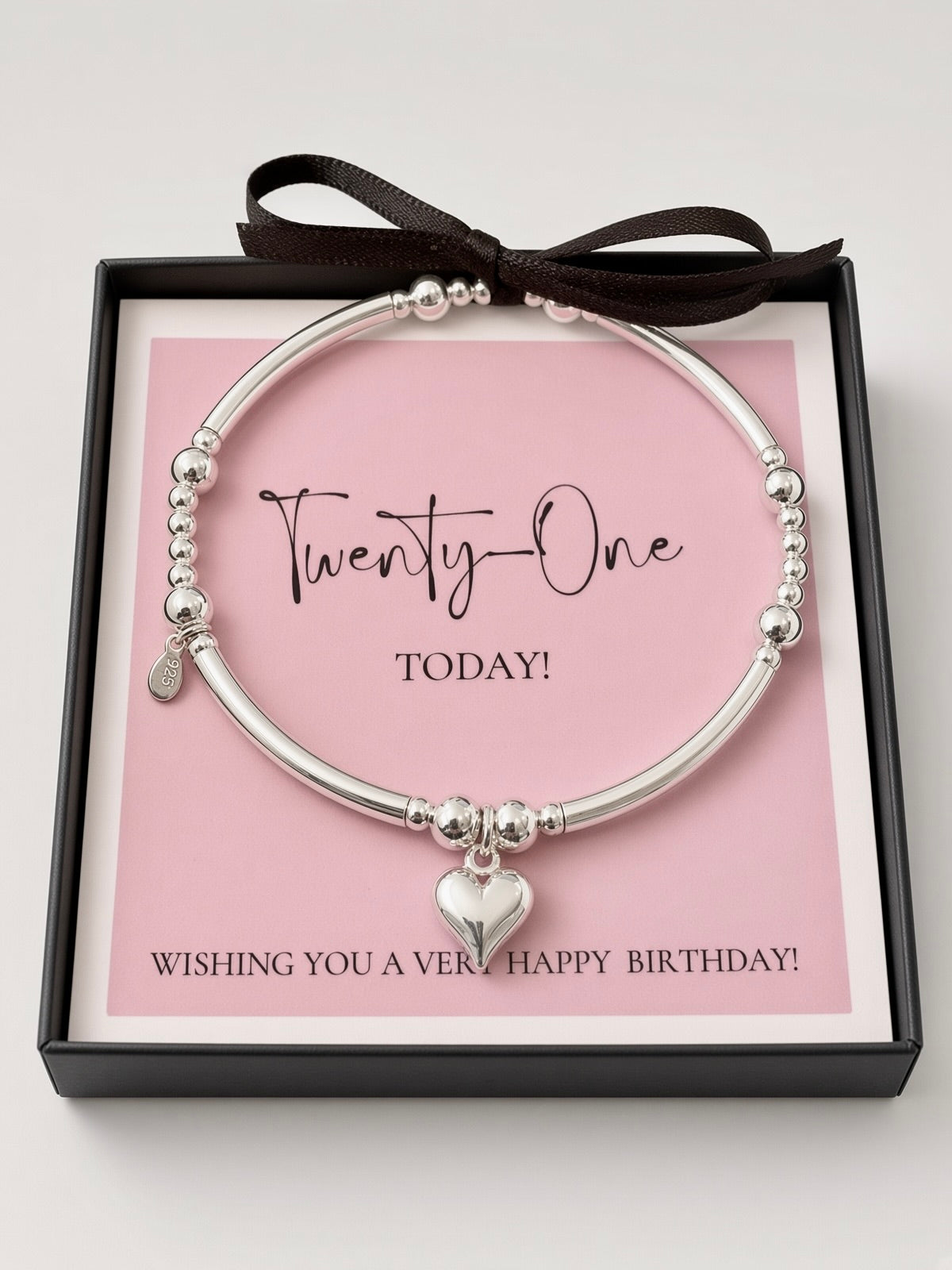 A silver beaded bangle bracelet with a heart charm, presented in a black gift box with a pink card that reads 'Twenty-One TODAY!' and 'Wishing you a very happy birthday!', tied with a black ribbon.
