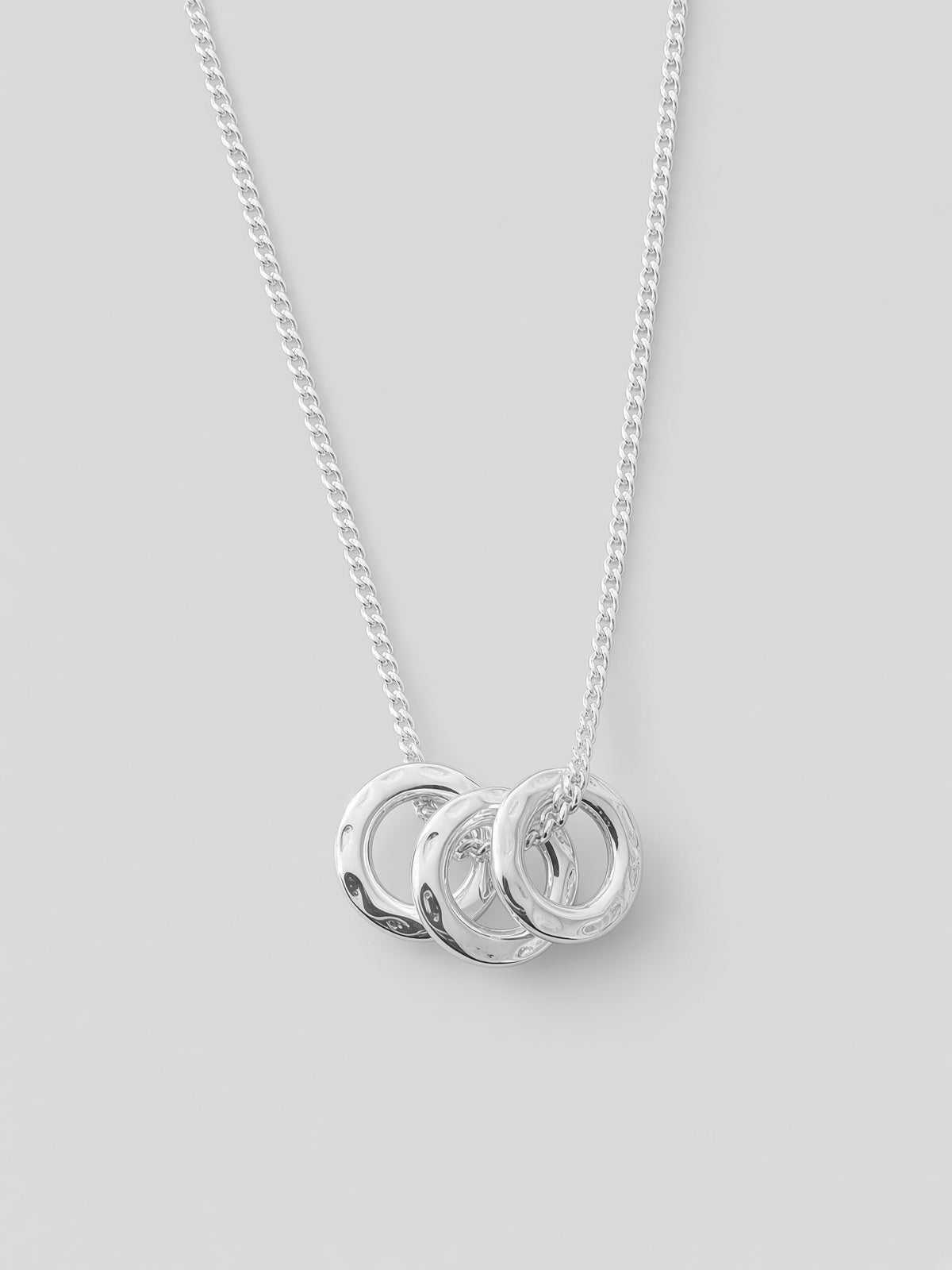 A silver chain necklace with three interlocking open circular pendant rings, photographed against a plain light gray background.