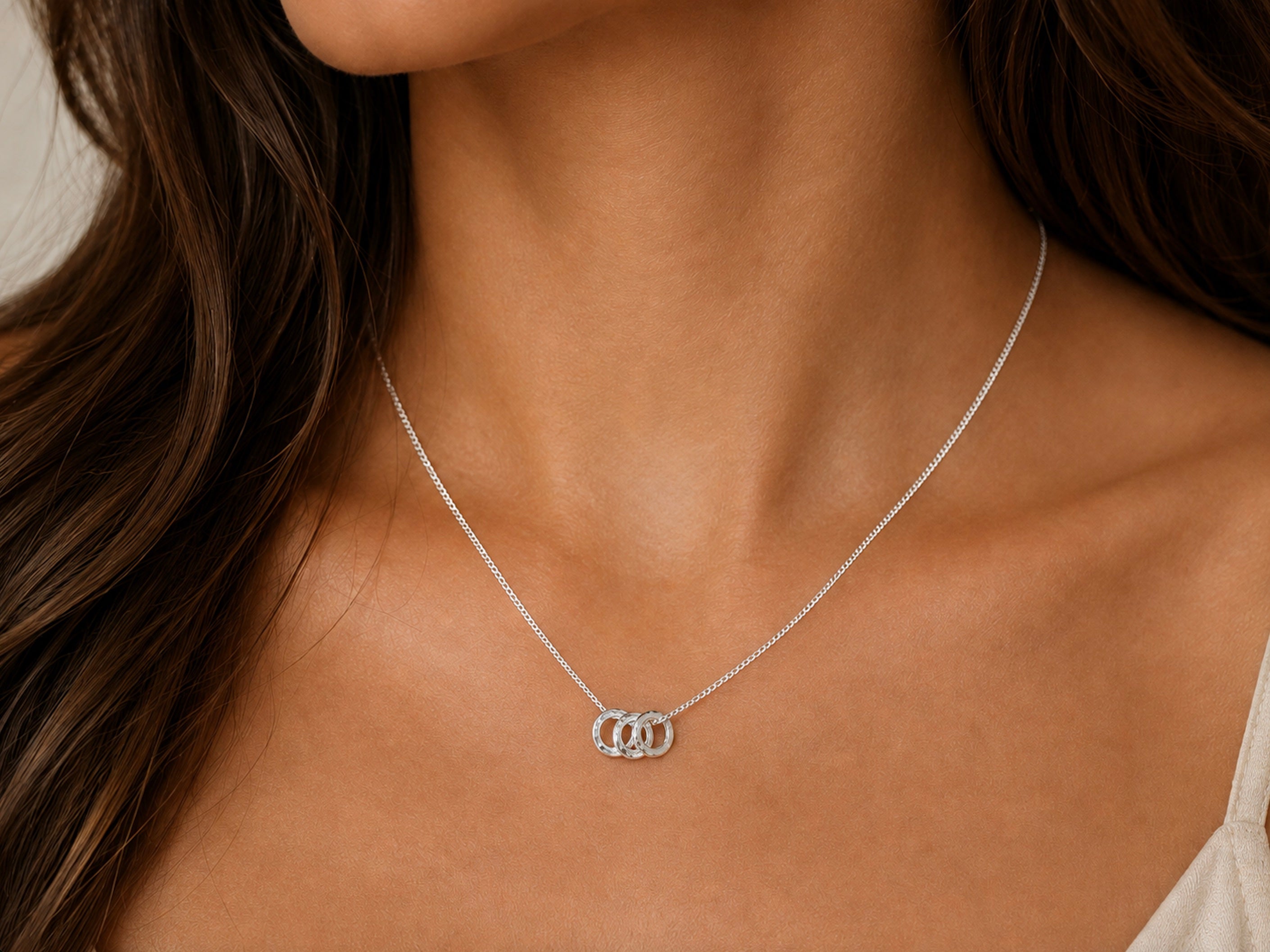 A close-up of a delicate silver 30th necklace gift.  3 rings for 3 decades jewellery. 