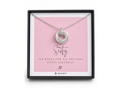 A silver ring pendant displayed inside a black gift box on a pink card that reads 'Sixty' and 'Six Rings for Six Decades. Happy Birthday!'.