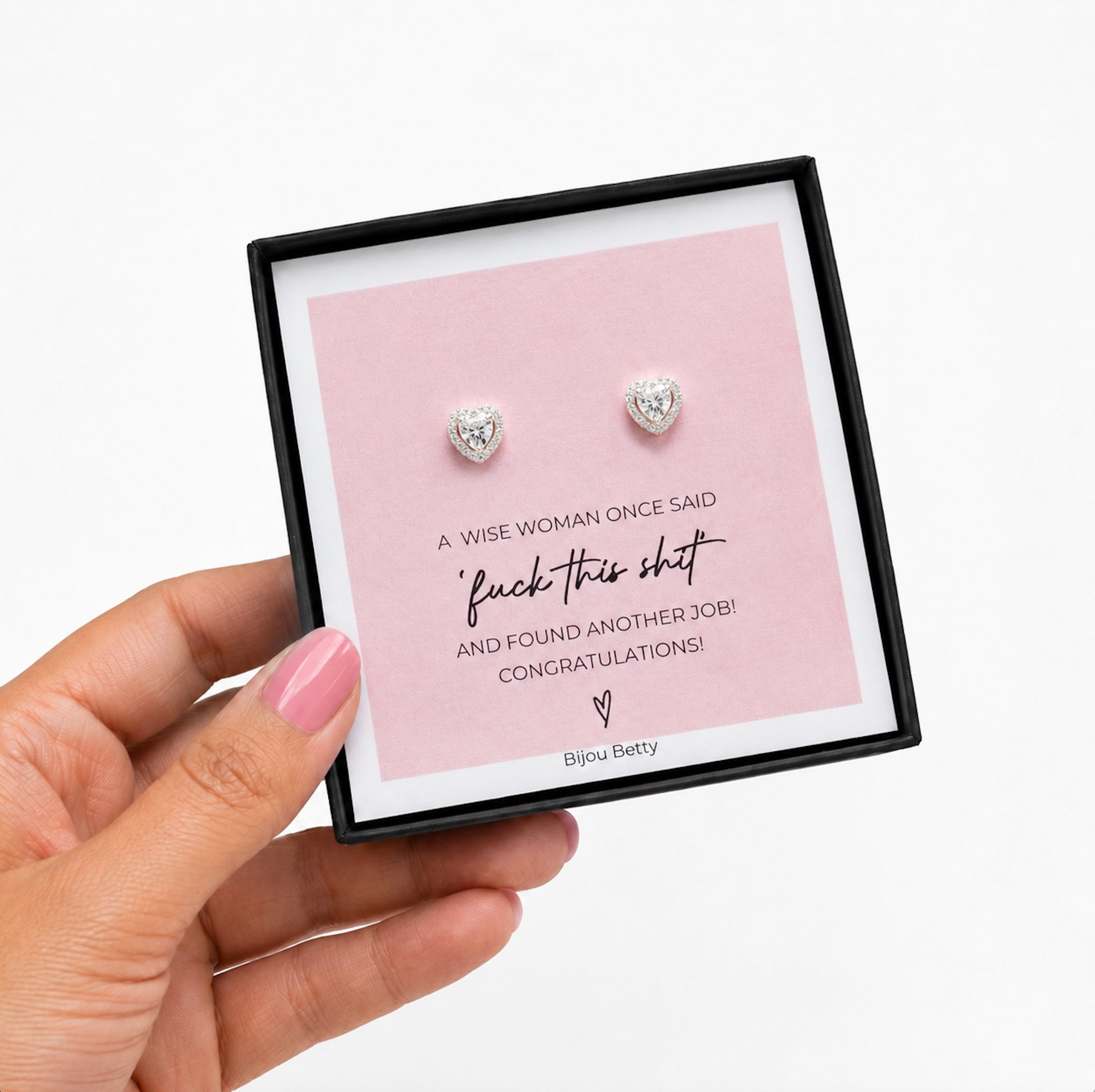 Heart-shaped earrings in a box with humorous message, held by a hand.