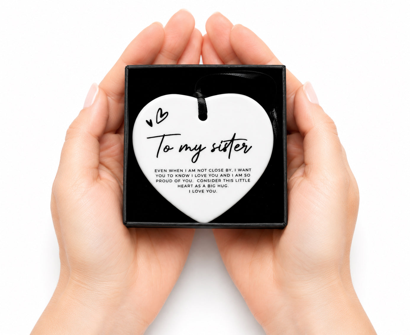 Heart-shaped pendant with 'To my sister' message held in hands on a white background