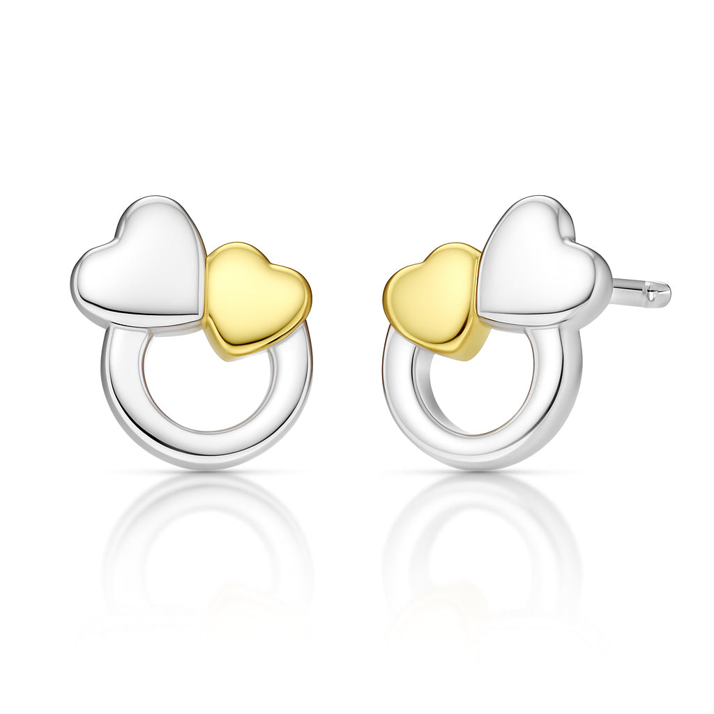 A pair of silver hoop earrings with a small white heart and a small yellow gold heart attached to each hoop, shown on a clean white background with a soft reflection below.