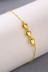 Gold bracelet with heart-shaped charms on a white surface
