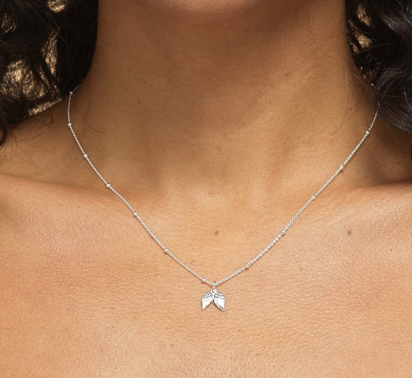 Close-up of model wearing Bijou Betty’s 925 silver angel wing necklace, 9mm x 10mm charm, styled for a comforting tribute.