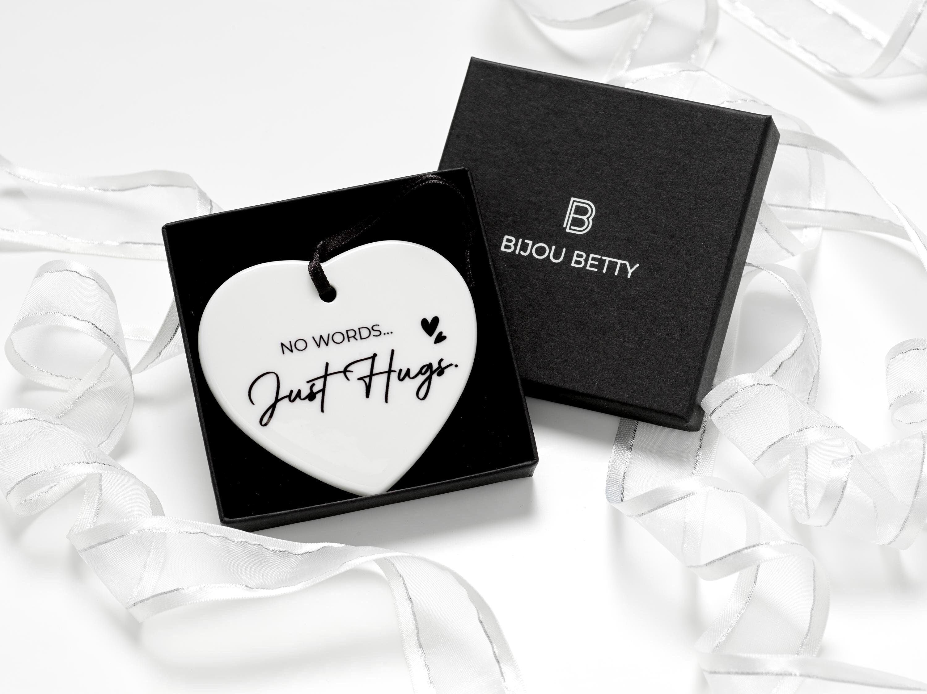 Ceramic heart keepsake with black satin ribbon, featuring the words No Words... Just Hugs. Perfect sympathy gift for family or friends during difficult times. Includes optional gift box, tissue paper, and personal message card.