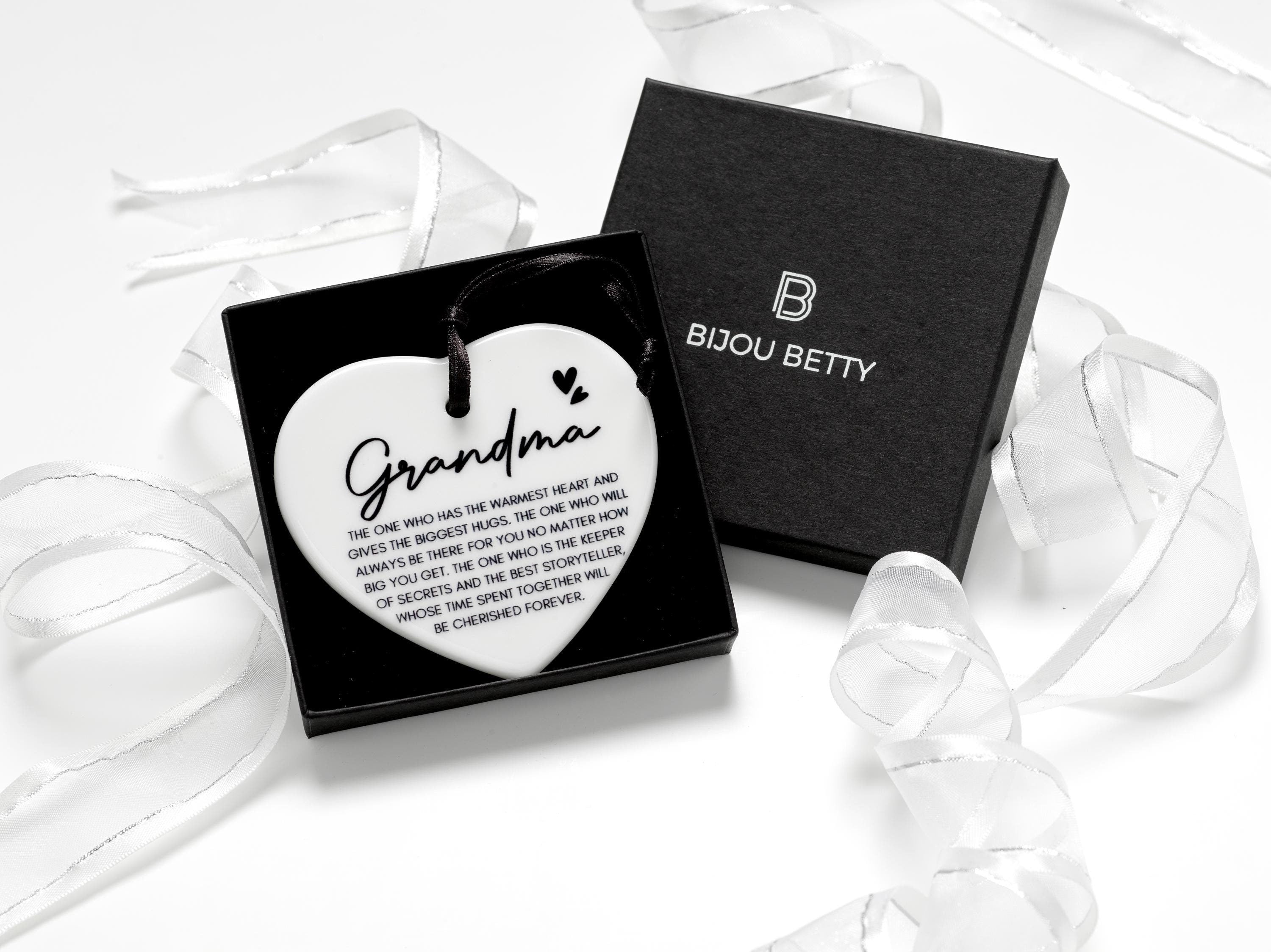 Ceramic heart keepsake with a black satin ribbon, featuring the heartfelt quote, Grandma - The one who has the warmest heart and gives the biggest hugs.  perfect for birthdays, Christmas, or as a sentimental gift for a cherished grandmother.