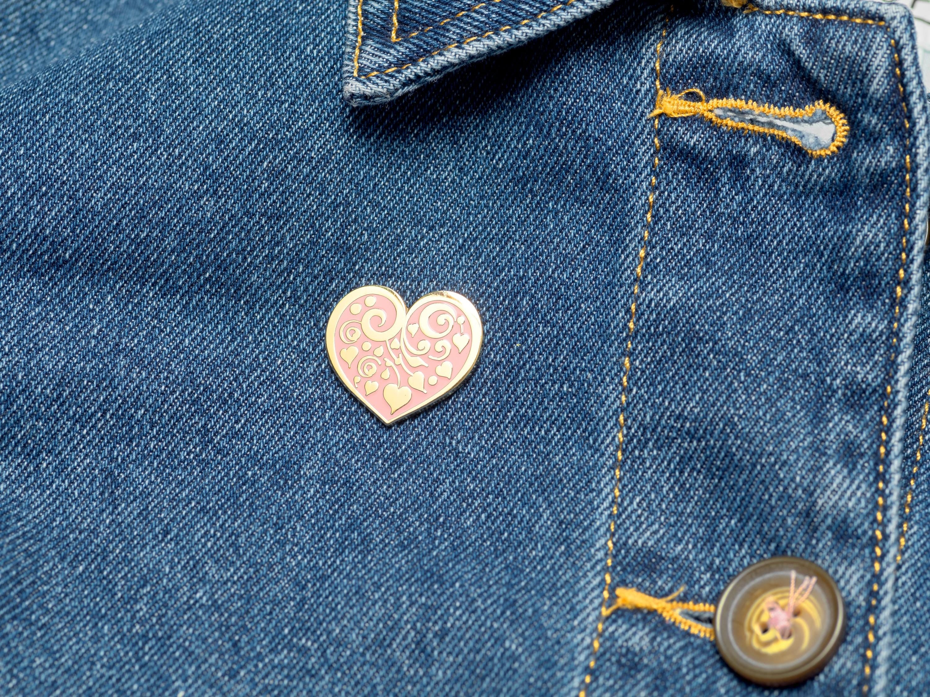 Bijou Betty’s gold-plated heart enamel pin with floral motif, pinned to a denim jacket, showcasing its 26mm x 25mm size.