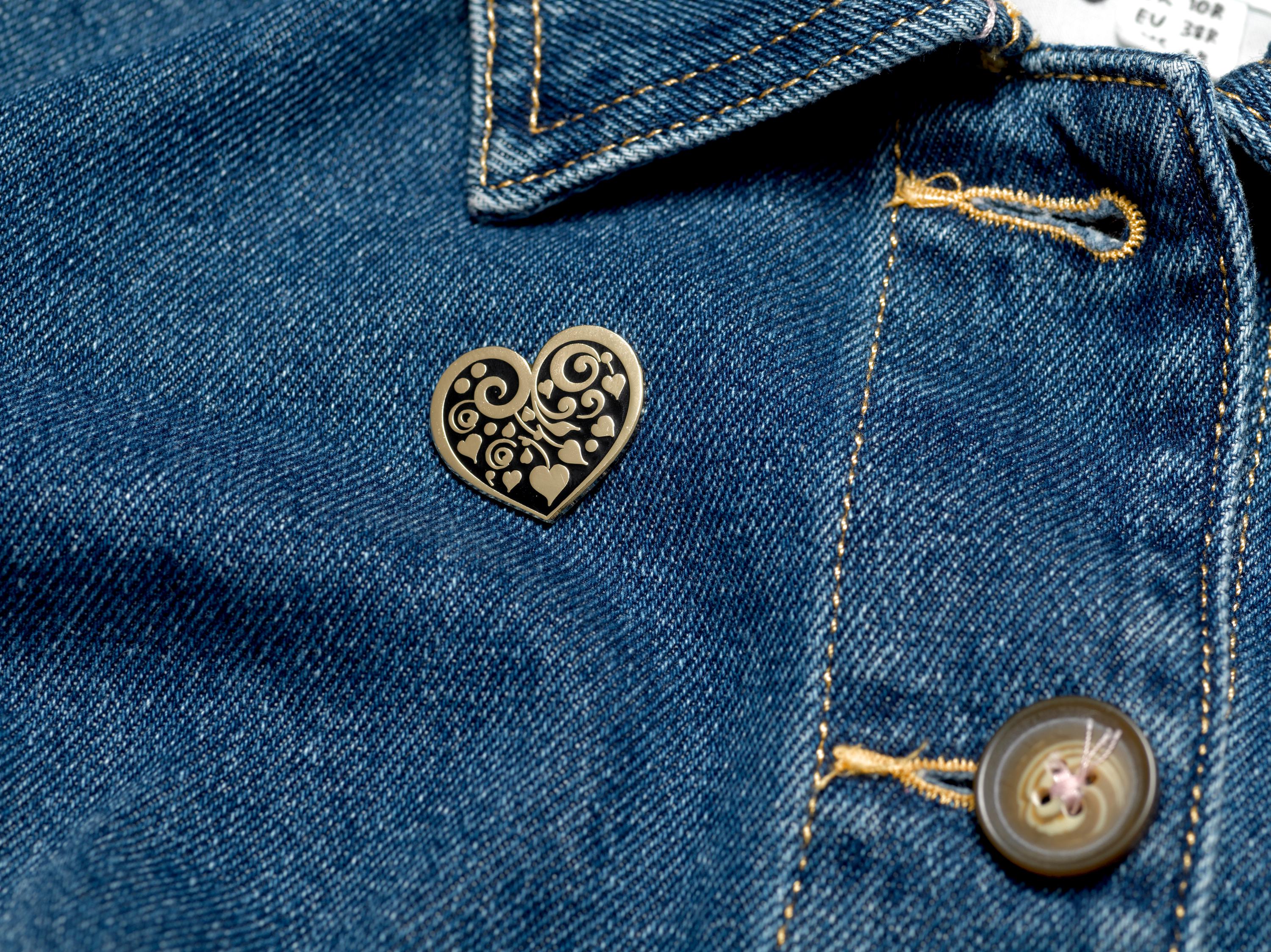 Bijou Betty’s gold-plated heart enamel pin with floral motif, pinned to a denim jacket, showcasing its 26mm x 25mm size.