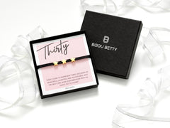 Black cord bracelet with three gold stars, adjustable for 30th birthday gift, in a gift box with tissue and card.