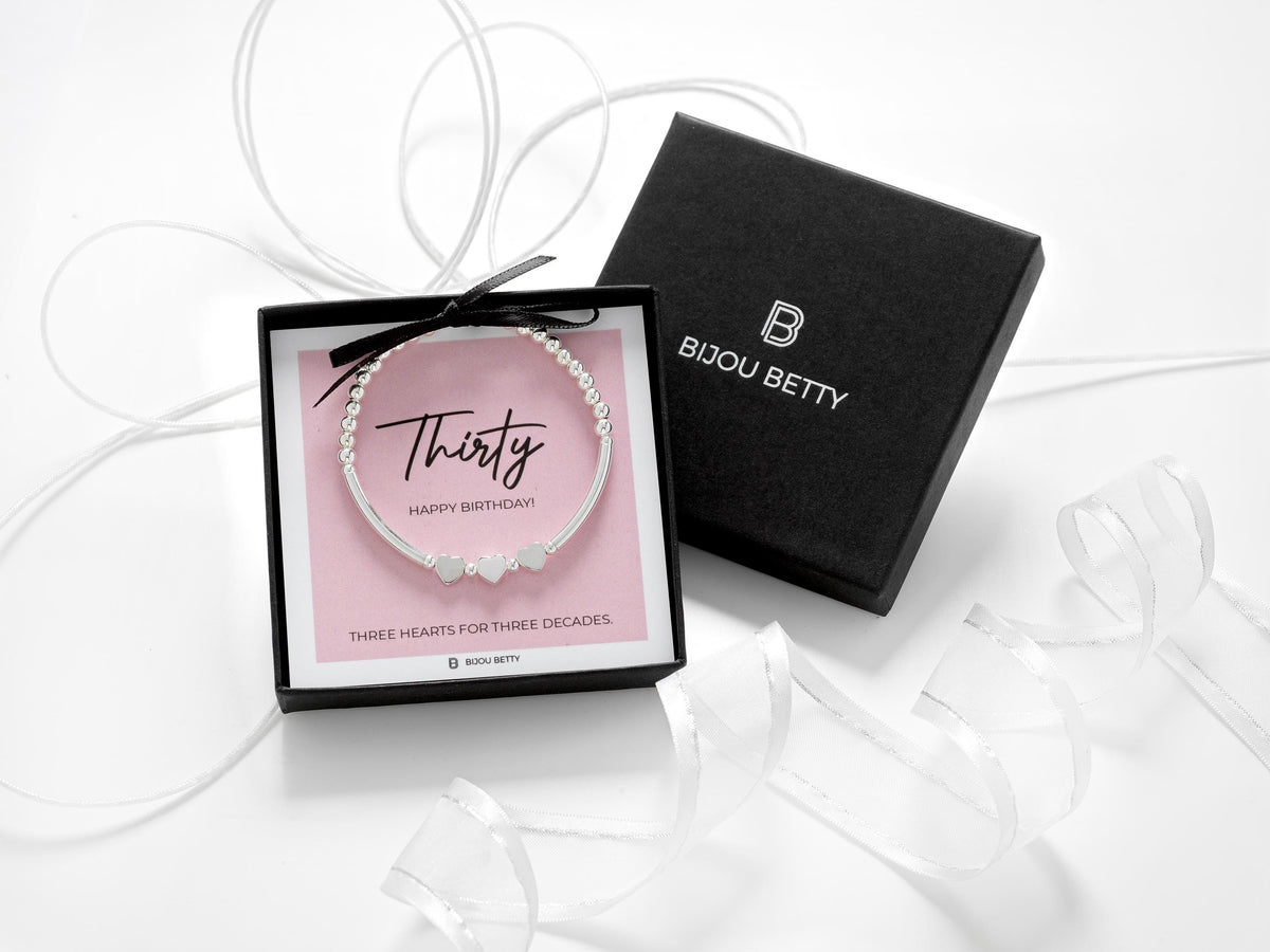 Sterling silver 30th birthday bracelet with three heart beads, dainty stretch design with polished silver beads, meaningful three decades gift for her, displayed on pink background, gift boxed jewellery by Bijou Betty